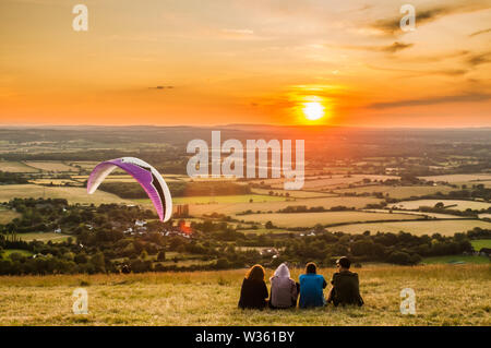 Devils Dyke, Brighton, East Sussex UK. 12th July 2019.. Last flight of the day into the strong Northerly wind as the sun sets over the countryside. . Stock Photo