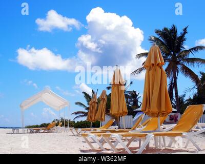 A row of folded yellow beach umbrellas and recliners on pure white sands, below a perfect blue sky with fluffy clouds, Shoal Bay East, Anguilla, BWI. Stock Photo