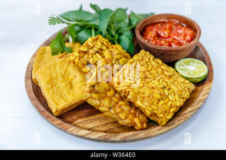 Fried tempeh and tofu served with spicy sambal sauce and lime. On a round wooden plate. Side view Stock Photo