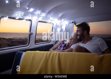 Couple sitting together in a camper van at beach during sunset Stock Photo