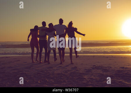 Friends with arms around walking towards the beach during sunset Stock Photo
