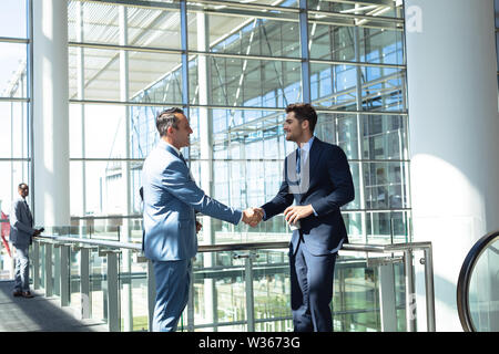Caucasian male executives shaking hands while standing in modern office Stock Photo