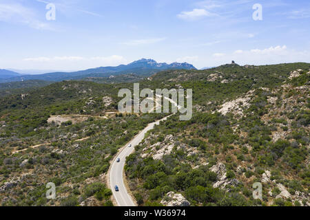 View from above, stunning aerial view of some cars that runs along a road flanked by a green forest. Sardinia, Italy. Stock Photo