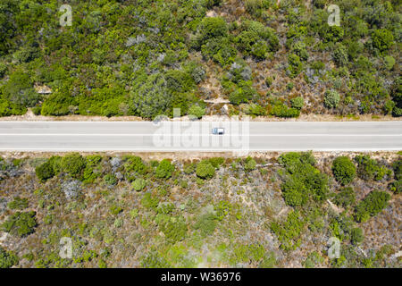 View from above, stunning aerial view of a car that runs along a road flanked by a green forest. Sardinia, Italy. Stock Photo