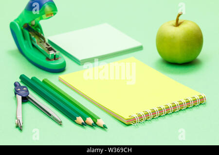 Compass, color pencils, notebook, apple, note paper and stapler on green background. Back to school concept. School supplies. Shallow depth of field. Stock Photo