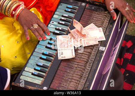 Close-up of a indian women's hand playing harmonium with ten rupees note on top of it, poor beggar concept - Image Stock Photo