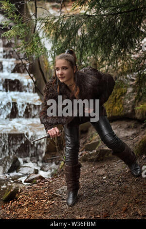 girl with a dagger with a dagger near a waterfall in a forest in the rain Stock Photo