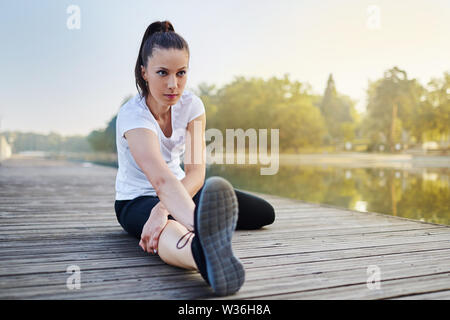 Portrait of young woman stretching near lake before jog in the morning Stock Photo