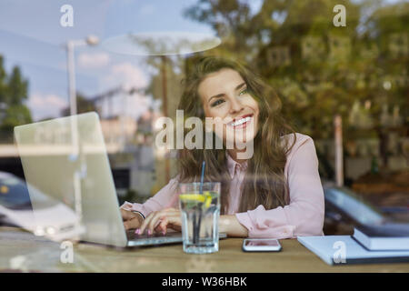 Happy young woman working on laptop in cafe Stock Photo