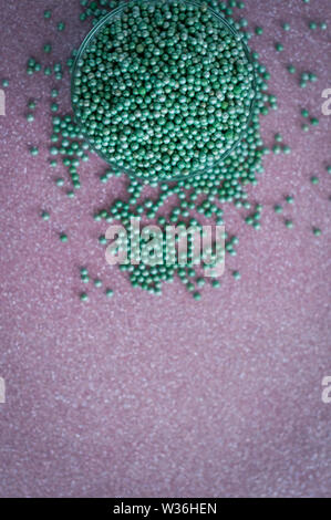 Green ball crystal sugar sprinkle dots, on glitter pink background, decoration for confectionery.  Sugar, sweetness, diabetes concept.