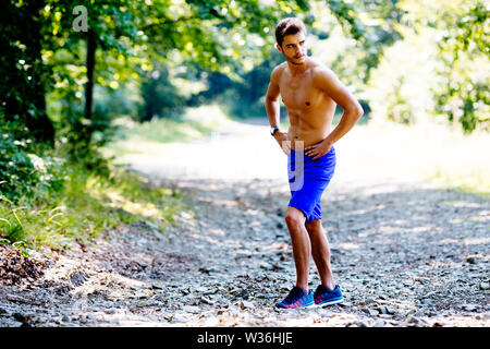 Muscular young man looking away while taking break from jogging in the mountains Stock Photo
