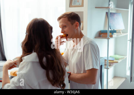 Blue-eyed husband biting apple while having breakfast with wife Stock Photo