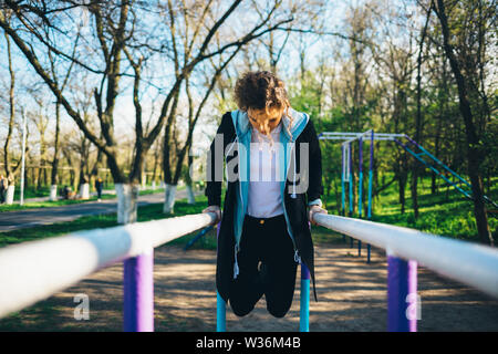 Young woman dressed in casual clothes exercising on parallel bars outdoors. Stock Photo