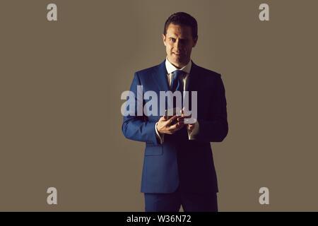 Happy businessman, man or manager smiling with mobile phone or smartphone in blue suit on grey background. Technology for business. Digital marketing, Stock Photo