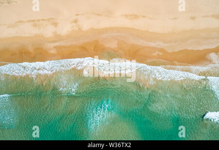Aerial top view of turquoise ocean wave reaching the coastline.