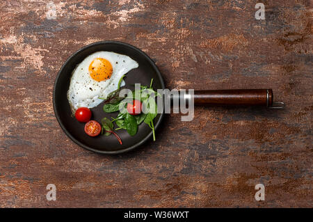 Pan with fried egg, cherry tomatoes and herbs on brown bronze background. Flat lay, top view, space for text Stock Photo