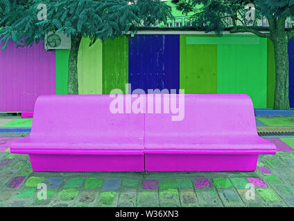 Pop art styled concrete bench in vibrant purple with green and blue wooden wall in the backdrop Stock Photo