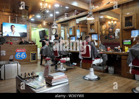 Barber cutting man's hair and men sitting in barbers chairs at Route 66 Barber Shop interior in Wellfield Road Cardiff Wales UK   KATHY DEWITT Stock Photo