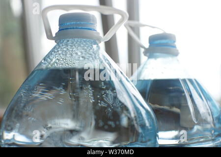 Two five-liter plastic bottles full of water, close-up of the top with lids and handles, condensation with drops inside the bottle Stock Photo