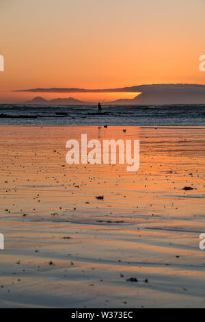 Orange beach sunset with fisherman silhouette and light reflecting off the wet beach sand. Stock Photo