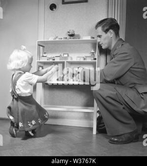 1940s girl playing. A young blonde girl is playing with her dollhouse. Her fathing is sitting beside her and joins in the game.  Sweden 1949.  Kristoffersson ref AT38-10 Stock Photo