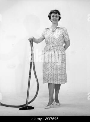 Cleaning day in the 1960s. A woman is standing holding a vacuum cleaner, looking happy. Sweden 1960s Kristoffersson ref CN109-10 Stock Photo