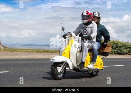 Morecambe, UK. 13th July, 2019. Morecambe Rides Again; The First Kick Scooter Collective and the Vespa Club of Morecambe (COG159) host a rally circuit in the resort which has the honour of being a Vespa Club Of Britain signing on event. Morecambe is back on the scootering map with the first proper scooter rally since the 1980s being held. Scooterists roared into town on their Vespas congregating at Happy Mount Park before a mass rally along the seafront promenade. Credit: Cernan Elias/Alamy Live News Stock Photo