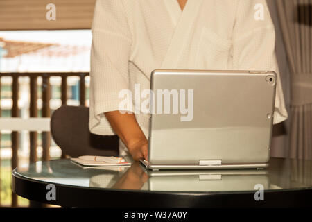 Businessman in bathrobe working on laptop in hotel room. Stock Photo