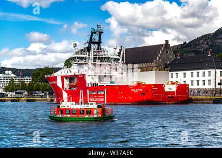 Offshore multi service standby rescue vessel Ocean Response in the port of Bergen, Norway. Small electric harbor ferry Beffen in front. Stock Photo