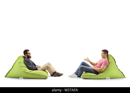 Full length profile shot of two men on bean bags having a conversation isolated on white background Stock Photo