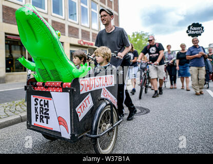Kiel, Germany. 13th July, 2019. Participants of the demonstration 'Initiative against Cruise Ships' and 'TKKG' will drive during the march through the city centre of Kiel with a cargo wheel with the inscription 'Stadtstrand statt Terminal' through the streets. The ships 'MSC Meraviglia', 'Mein Schiff 1' and 'Aidaprima' will dock in Kiel on 13 July. Credit: Axel Heimken/dpa/Alamy Live News