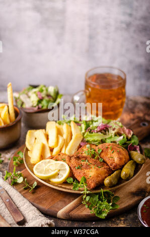 Delicious breaded meat with french fries, salad, pickless and beer Stock Photo