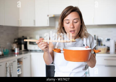 Young woman tasting food in the home kitchen