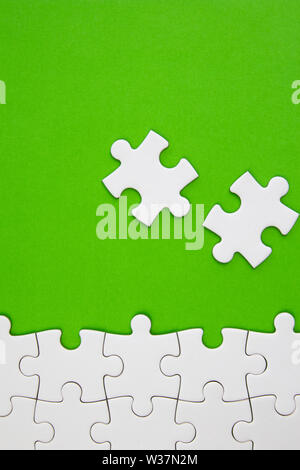 White jigsaw puzzle pieces on green background with negative space Stock Photo