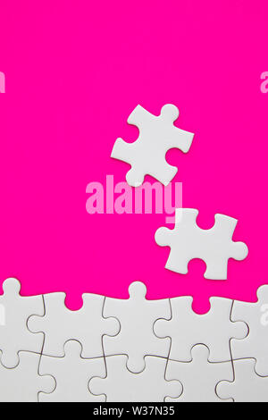 White jigsaw puzzle pieces on pink background with negative space Stock Photo
