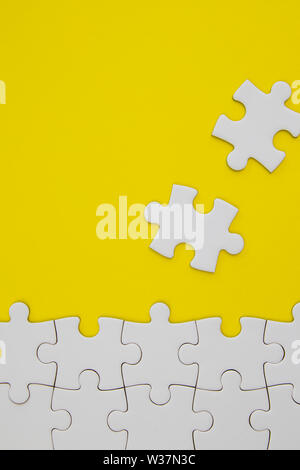 White jigsaw puzzle pieces on yellow background with negative space Stock Photo