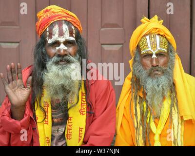 Two old Nepali Vaishnavite sadhus (holy men who worship Vishnu) with painted foreheads wear traditional red and yellow outfit and pose for the camera. Stock Photo