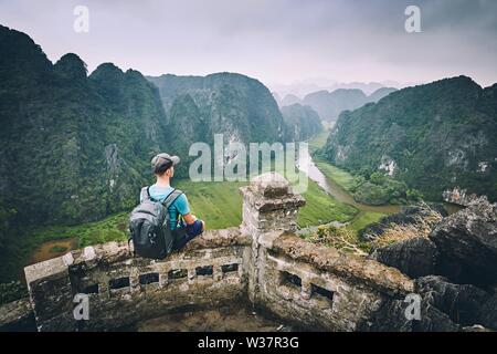 Traveler in Vietnam. Pensive Young man with backpack sitting on peak Mua Cave. Ninh Binh province, Vietnam. Stock Photo