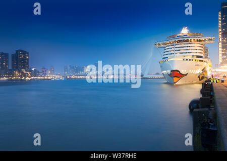 A cruise ship is anchoring in Rotterdam. It is the glowing Aida Prima at night. In the background is the famous Erasmusbrug. Stock Photo