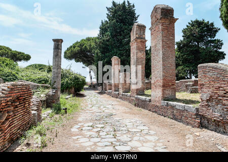 Roman empire street view with ruins and roman columns and typical cobblestone road at Ostia Antica - Rome Stock Photo