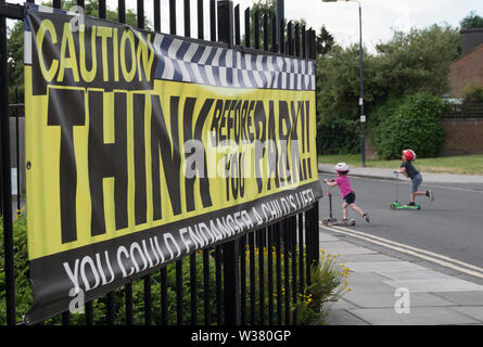 small children ride scooters beside a think before you park, sign aimed at drivers outside a school in twickenham, middlesex, england Stock Photo
