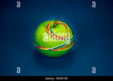 Green apple tied in colorful rubber bands over a blue background. Simplicity back to school or diet, aerobic concept with copy space for text Stock Photo