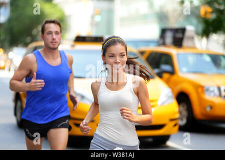 Active couple running on famous shopping street fifth avenue in Manhattan, New York City NYC, USA. Exercise lifestyle portrait of young asian woman runner and caucasian male jogger. Stock Photo
