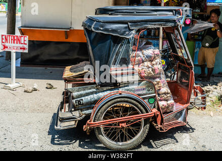 Puerto Princesa, Palawan, Philippines - March 3, 2019: Street view. red-black motor-tricycle taxi filled with merchandise to be delivered. People in b Stock Photo