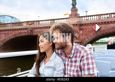 Couple travel in Berlin sightseeing on boat tour. Beautiful young multiracial adults relaxing on a cruise visiting the city on a day boating excursion for tourists. Stock Photo
