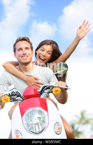 Couple driving scooter having fun in love and happy together. Joyful mixed race young couple together outside driving motorcycle scooter. Interracial couple, Asian woman, Caucasian man. Stock Photo