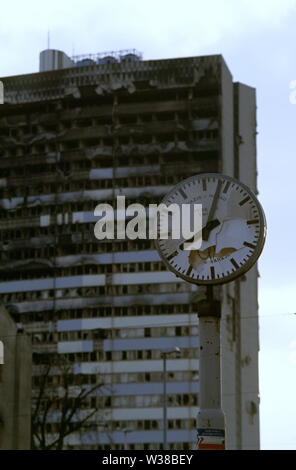2nd April 1993 During the Siege of Sarajevo: the burned-out upper floors of the Assembly Building form the backdrop to a broken street clock. Stock Photo