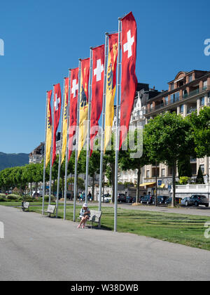 A tourist sitting under the Geneva flags and the Swiss flags floating in the wind on the Quay Mont-Blanc Stock Photo