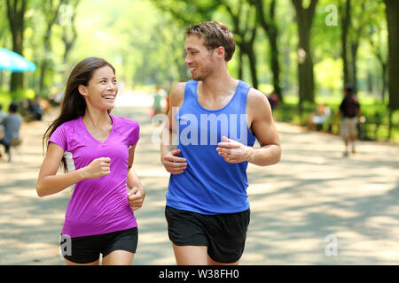 Running couple training in Central Park, New York City (NYC). Happy runners talking together during run on famous Mall walk path under trees in Manhattan, urban fitness. Stock Photo