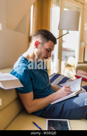 A handsome man is taking notes while learning from the book Stock Photo